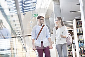 Smiling couple holding hands while talking by library at university