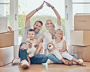 Smiling couple with little kids sitting and making symbolic roof with hands over children. Cheerful family sitting