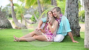 Smiling Couple In Love with Lei, Sitting And Hugging under palm tree