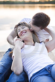 Smiling couple lying on the bridge on the shore of the lake at sunset