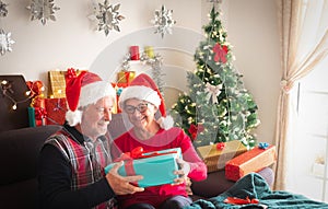 A smiling couple of man and woman in Santa`s hats with many presents for them and for family. Christmas tree on the background