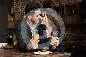 smiling couple with orange juice going to kiss