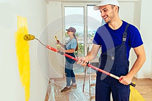 Smiling couple painting wall with paint roller and paintbrush at