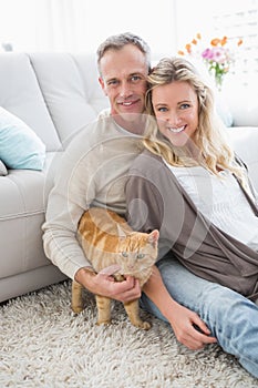 Smiling couple petting their gringer cat on rug