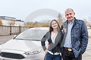 Smiling couple posing near new car with keys