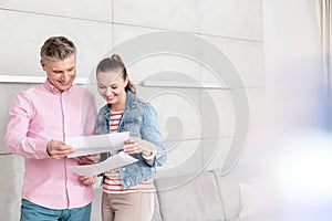 Smiling couple reading agreement paper while standing against wall in apartment