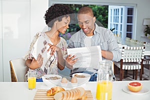 Smiling couple reading magazine and documents during breakfast