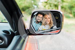 smiling couple reflecting in car mirror and looking