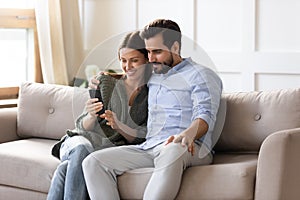 Smiling couple relax at home using smartphone gadget