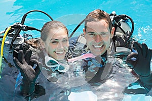 Smiling couple on scuba training in swimming pool showing ok gesture