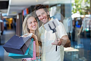 Smiling couple with shopping bags taking selfies with selfiestick