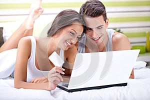 Smiling couple shopping online while lying on their bed