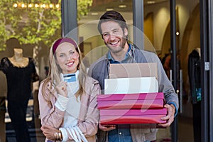Smiling couple showing credit card and carrying boxes