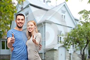 Smiling couple showing thumbs up over house