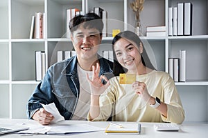 Smiling couple sitting and managing bills at home, paying by credit card. Happy man and woman pay bills and manage