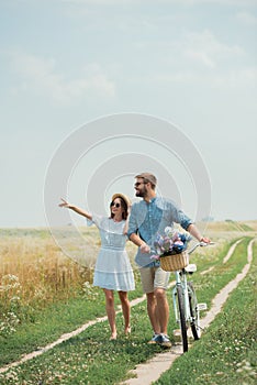 smiling couple in sunglasses with retro bicycle in summer field