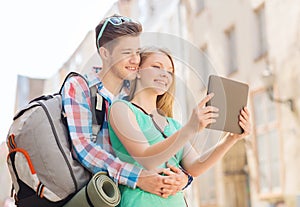 Smiling couple with tablet pc and backpack in city