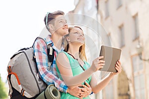 Smiling couple with tablet pc and backpack in city