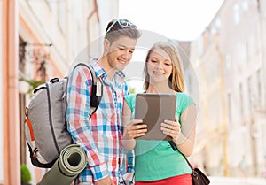 Smiling couple with tablet pc and backpack in city