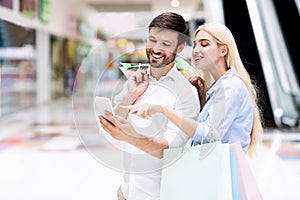 Smiling Couple Using Cellphone Searching Sales Offers Standing In Mall