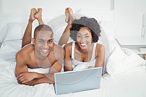 Smiling couple using laptop on bed