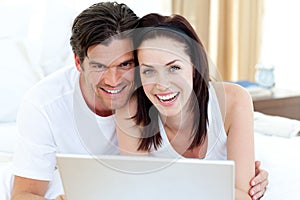 Smiling couple using a laptop lying on their bed