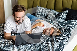 Smiling young couple using a laptop lying on their bed