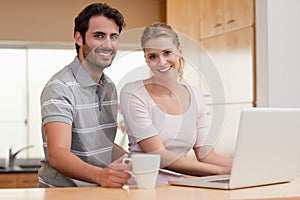 Smiling couple using a notebook while having coffee