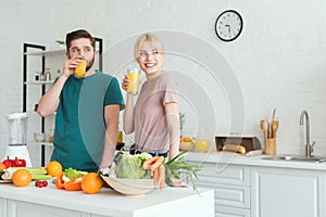 smiling couple of vegans drinking fresh juice at kitchen