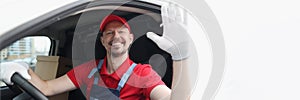 Smiling courier driver in car cab waving his hand in greeting