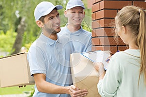 Smiling couriers in blue uniforms and young women filling up delivery documents