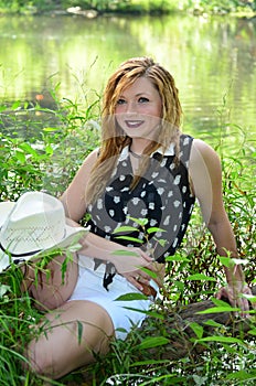 Smiling Cowgirl Sitting On Log by the Lake