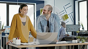 Smiling coworkers in office looking at laptop screen comparing business analytics with sales charts