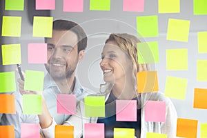 Smiling coworkers writing tasks on sticky papers, post it notes