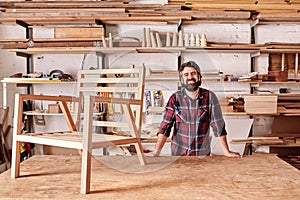 Smiling craftsman in his woodwork studio with wooden chair frame