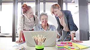 Smiling creative director looking at laptop with his team and discussing plans