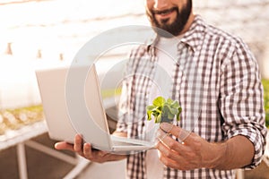 Smiling crop gardener with lettuce and laptop in hothouse