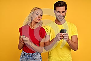 Smiling curious young couple friends guy girl in colored t-shirts posing isolated on yellow background studio. People lifestyle