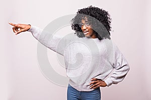 Smiling curly african woman pointing away and looking at the camera over white background