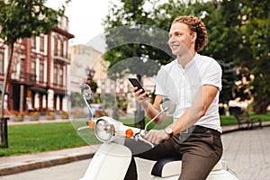 Smiling curly business man holding smartphone and looking away