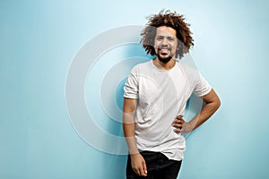 Smiling curly-headed man in white T-shirt with a hand on the hip. An easy going person with positive outlook. Happiness