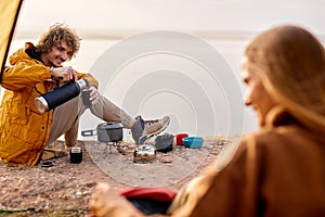 Smiling curly man puring tea into cup from thermos, smiling, enjoy travel