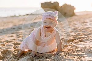 Smiling cute baby girl in outdoor with sunset. Happy child in pink dress on ocean beach