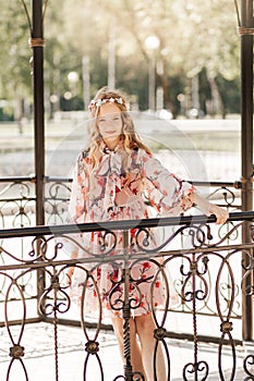 Smiling cute blonde teen girl posing in summer garden. Wearing flower wreath outdoors