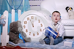 Smiling cute boy holding his present during christmas time. big white clock and teddy bear on background