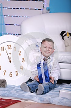 Smiling cute boy holding his present during christmas time. big white clock and teddy bear on background