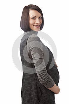 Smiling Cute Caucasian Brunette Pregnant Woman in Grey Long Dress Standing Over Pure White Background And Looking To Camera