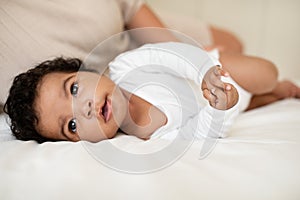Smiling cute curly african american little child in soft clothes lie on white bed, relax, sleep time in bedroom interior