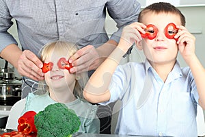 Smiling cute daughter and son cooking a dinner. Little children playing with colorful pepper with father.