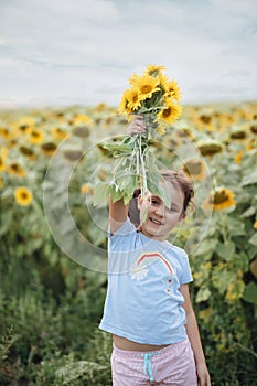 Smiling cute girl holding over head bouquet of sunflowers on field. Summer holiday